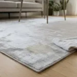 Close-up of a soft gray viscose area rug with a faint tan water spot on a wood floor
