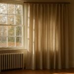 Lined drapes beside tall multi-pane windows in an older home living room, lit by soft autumn sun